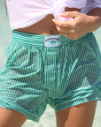 Maison Paddle striped boxer shorts worn at the beach, close-up waistband shot styled for post-padel relaxation.